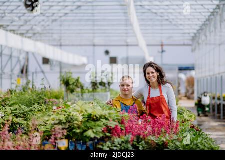 Erfahrene Frau Floristin hilft jungen Angestellten mit Down-Syndrom im Gartencenter. Stockfoto