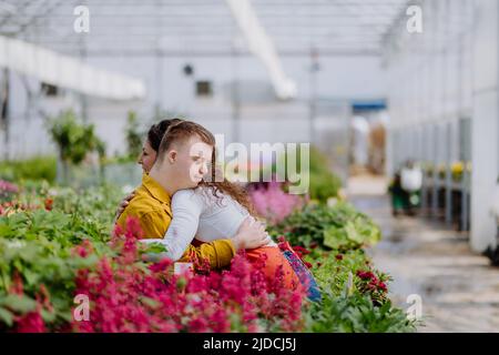 Frau Floristin umarmt ihren jungen Kollegen mit Down-Syndrom in Gartencenter. Stockfoto