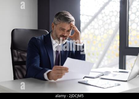 Geschäftliche Probleme. Besorgter Geschäftsmann Mittleren Alters, Der Dokumente Im Büro Liest Stockfoto