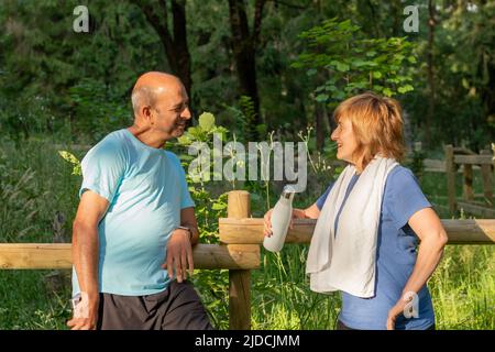 Ältere Männer und Frauen, die sich gegenseitig anblicken und sich nach dem Arbeiten in einer natürlichen grünen Umgebung unterhalten und lächeln Stockfoto