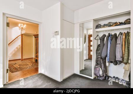 Vintage-Schrank mit Dekorationen und Spiegel in der Nähe offene Wohnzimmertür und Treppe im Flur des Hauses Stockfoto