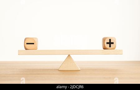 Plus- und Minus-Balance-Konzept. Positive und negative Symbole auf Holzblöcken sind auf einer hölzernen Wippe im Gleichgewicht. Speicherplatz kopieren Stockfoto