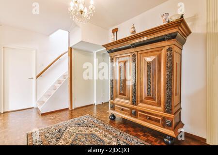 Vintage-Schrank mit Dekorationen und Spiegel in der Nähe offene Wohnzimmertür und Treppe im Flur des Hauses Stockfoto