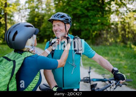 Aktives Seniorenpaar, das im Sommerpark Fahrrad fährt, Helm aufsetzt, gesundes Lifestyle-Konzept. Stockfoto