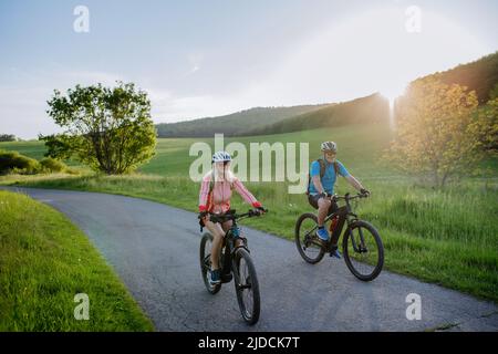 Aktives Seniorenpaar, das auf der Straße im Sommerpark Elektrofahrräder fährt, gesundes Lifestyle-Konzept. Stockfoto