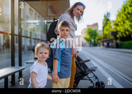 Die junge Mutter pendler mit kleinen Kindern auf dem Weg zur Schule und wartet in der Stadt auf den Bus. Stockfoto