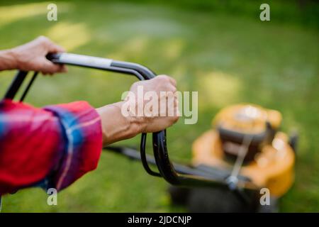 Nahaufnahme einer älteren Frau, die mit einem Rasenmäher im Garten Gras mäht, Konzept für Gartenarbeit. Stockfoto