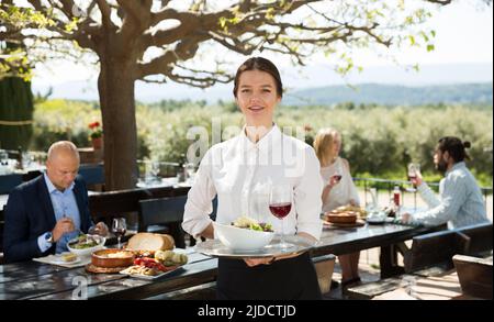 Positive Frau Kellner demonstrieren open-air Restaurant für Besucher Stockfoto