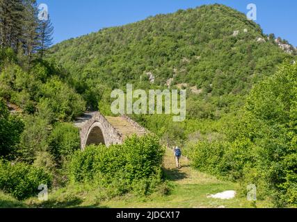 Ein Wanderer, der die Hatsios-Brücke über den Vikakis-Fluss überquert, bevor er in die Vikakis-Schlucht - Zagori-Region des Pindus-Gebirges Griechenland eindringt Stockfoto