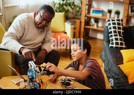 Ein Großvater und ein Enkel bauen zu Hause einen Roboter zusammen. Ausbildung in Robotik und Elektronik. Stockfoto