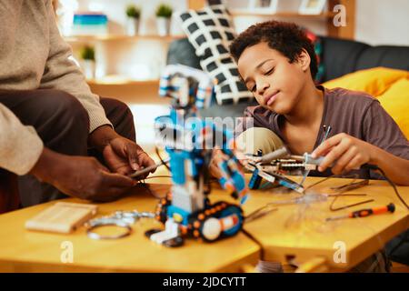 Ein Großvater und ein Enkel bauen zu Hause einen Roboter zusammen. Ausbildung in Robotik und Elektronik. Stockfoto