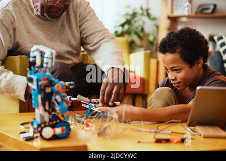 Ein Großvater und ein Enkel bauen zu Hause einen Roboter zusammen. Ausbildung in Robotik und Elektronik. Stockfoto