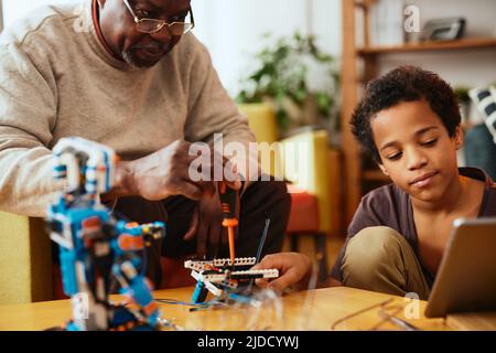 Ein Großvater und ein Enkel bauen zu Hause einen Roboter zusammen. Ausbildung in Robotik und Elektronik. Stockfoto