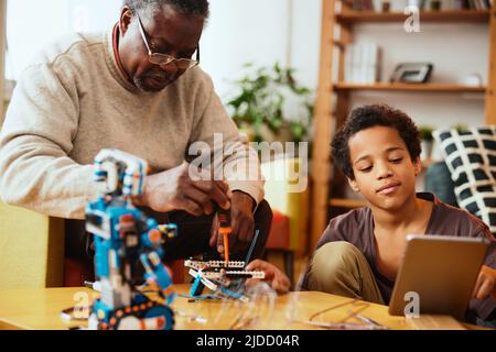 Ein Großvater und ein Enkel bauen zu Hause einen Roboter zusammen. Ausbildung in Robotik und Elektronik. Stockfoto