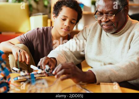 Ein Großvater und sein Enkelkind bauen zu Hause einen Roboter. Stockfoto