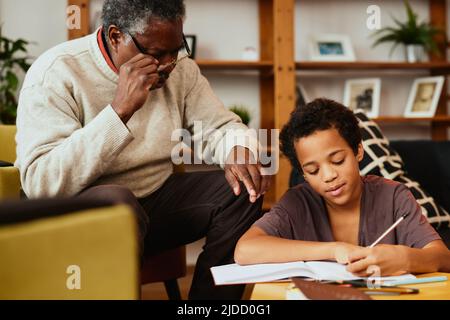 Intelligenter afrikanischer Junge, der seine mathematischen Hausaufgaben mit ein wenig Hilfe seines Opa macht. Nachhilfe und Bildung Stockfoto