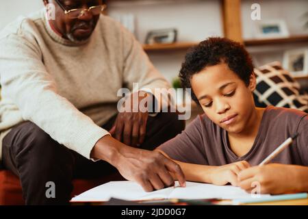 Intelligenter afrikanischer Junge, der seine mathematischen Hausaufgaben mit ein wenig Hilfe seines Opa macht. Nachhilfe und Bildung Stockfoto