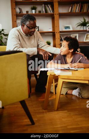 Ein afrikanischer Großvater, der seinem Enkel zeigt, wie man ein mathematisches Problem löst. Unterstützung durch die Familie Stockfoto