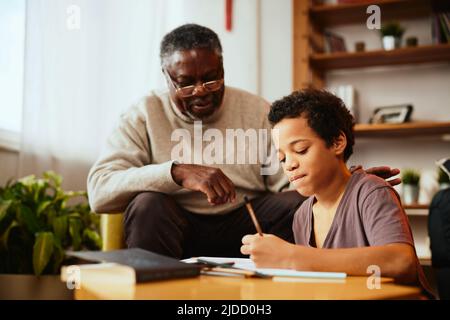 Ein afrikanischer Großvater, der seinem Enkel zeigt, wie man ein mathematisches Problem löst. Unterstützung durch die Familie Stockfoto