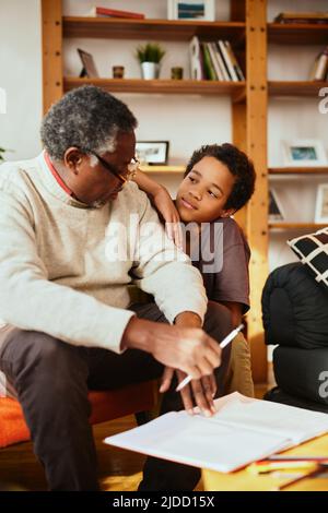 Ein afroamerikanischer Großvater sitzt zu Hause mit seinem Enkel und erklärt ihm ein mathematisches Problem. Stockfoto