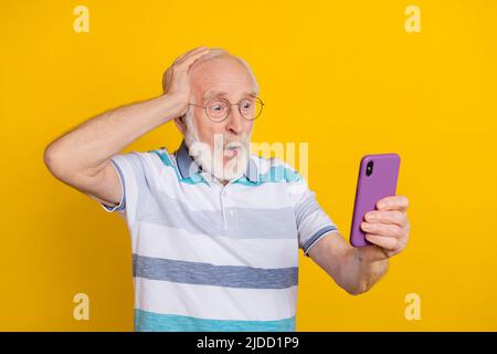 Portrait von attraktiven wunderten grauhaarigen Mann mit Gadget Wow Reaktion Nachrichten isoliert über helle gelbe Farbe Hintergrund Stockfoto