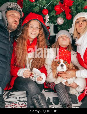 Glückliche Familie Vater Mutter 2 Mädchen geben Ihnen weht Kuss. Weihnachtsfeier im Auto LKW. Rote Weihnachtsdekoration. Fröhliche Stimmung. Glück. Stockfoto