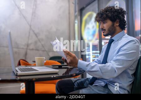 Mann, der seitlich zur Kamera sitzt und Papiere studiert Stockfoto