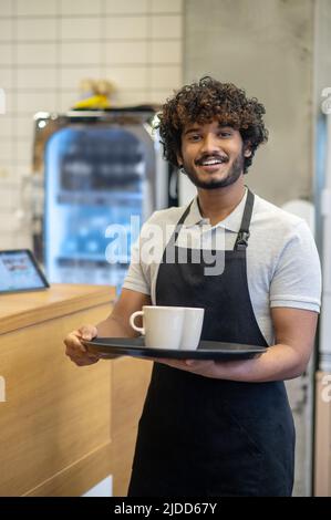 Mann hält Tassen auf dem Tablett und lächelt der Kamera zu Stockfoto
