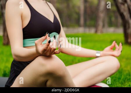 Nette kaukasische Frau trägt sportliche Kleidung im Stadtpark, im Freien tun Yoga bequeme Sitzposition, sukhasana Haltung entspannen atmen einfache Sitzposition, Gesundheit Stockfoto