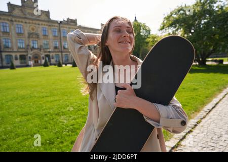 Lady mit geschlossenen Augen steht im Park mit Skateboard in den Händen Stockfoto