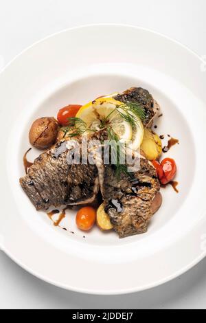 Gebratenes, frisches Seebarschfilet mit Kartoffeln und Gemüse auf weißem Hintergrund Stockfoto