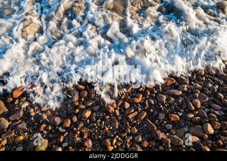 Kleine rote Kieselsteine, die von Wellen an einem Strand in Las Flores, Maldonado, Uruguay, gewaschen werden Stockfoto
