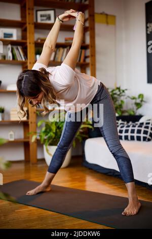Eine flexible Yogi-Frau mittleren Alters, die zu Hause auf einer Yogamatte steht und Yoga praktiziert. Yogi Frau macht Yoga-Übungen zu Hause. Stockfoto