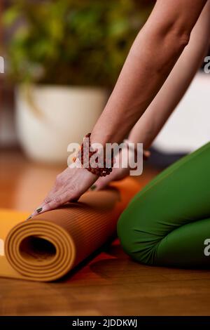 Nahaufnahme der Hände einer Yogi-Frau, die zu Hause eine Yogamatte hochrollt. Die Hände Rollen Yogamatte. Stockfoto