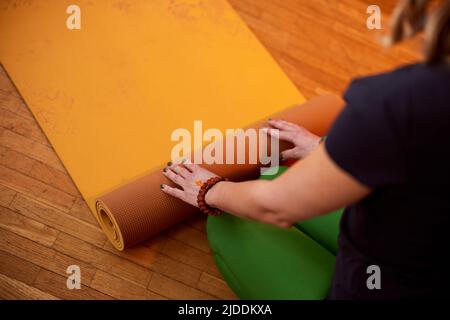 Nahaufnahme der Hände einer Yogi-Frau, die zu Hause eine Yogamatte hochrollt. Die Hände Rollen Yogamatte. Stockfoto