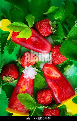 Hausgemachtes Erdbeereis oder Eis, Eis, Erdbeerblätter und Beeren. Gefrorener Fruchtsaft, Blick von oben. Sommerlich saftige Tapete. Stockfoto