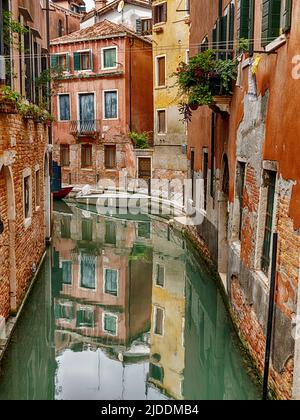 Ruhiges Wasser in einem engen Kanal von Venedig spiegelt die Gebäude auf beiden Seiten wider. Stockfoto