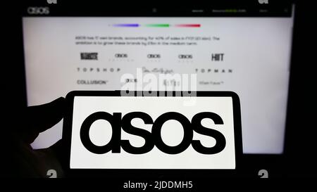 Person, die ein Smartphone mit dem Logo des britischen Modehandels ASOS plc auf dem Bildschirm vor der Website hält. Konzentrieren Sie sich auf die Telefonanzeige. Stockfoto