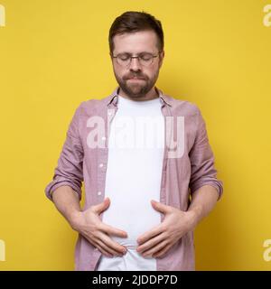 Übergewichtiger Mann hält sein überschüssiges Bauchfett mit den Händen und schließt die Augen frustriert. Konzept der richtigen Ernährung und einer gesunden Lebensweise. Stockfoto