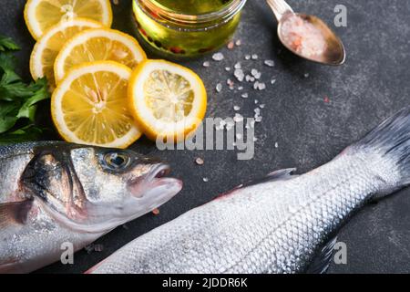 Seebarsch roh. Frischer Meeresfischbarsch mit Salz, Pfeffer, Petersilie, Olivenöl und Zitrone auf dunklem Beton auf rustikalem Hintergrund. Frischer Fisch bereit zum Kochen. Essen c Stockfoto