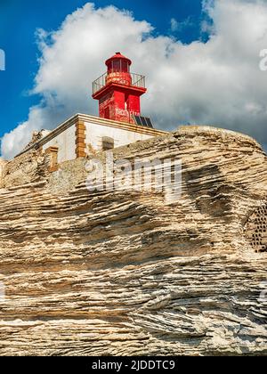 Dieser leuchtend rote Leuchtturm steht hoch auf einem felsigen Punkt außerhalb des Hafens von Bonifacio. Stockfoto