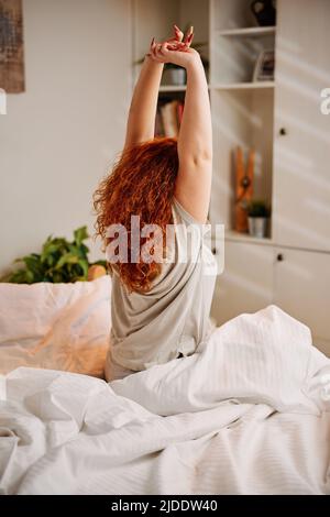 Ein Rotschopf-Mädchen wacht am Morgen auf und streckt ihre Arme. Stockfoto