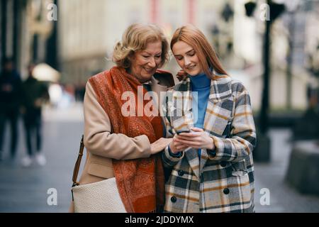 Eine Großmutter und ihr Enkelkind stehen auf der Straße und lesen Nachrichten am Telefon. Stockfoto