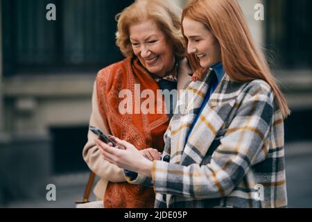 Eine Großmutter und ihr Enkelkind stehen auf der Straße und lesen Nachrichten am Telefon. Stockfoto