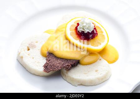 Sirloin-Sahnesauce mit Knödeln, serviert mit Zitrone, Preiselbeeren und Schlagsahne Stockfoto