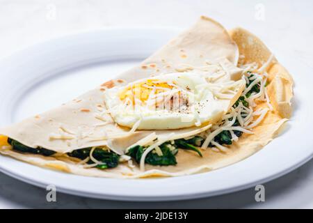 Pfannkuchen gefüllt mit Spinatblättern, serviert mit Spiegelei und geriebenem Käse Stockfoto