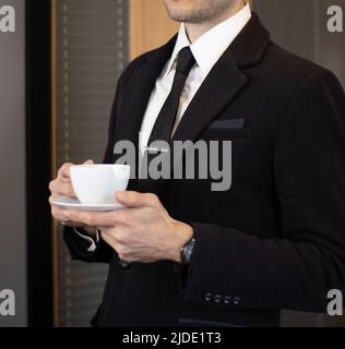 Geschäftsmann im schwarzen Anzug, der im Büro Kaffee trinkt Stockfoto
