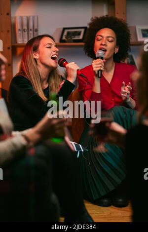 Multikulturelle Gruppe von Freunden, die am Mikrofon singen und zu Hause Karaoke-Abend haben. Stockfoto