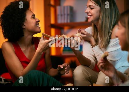 Glückliche multikulturelle Freundinnen, die zu Hause feiern und Pizza essen. Stockfoto