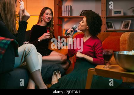 Eine afrikanische Frau, die zu Hause sitzt und auf einer Karaoke-Party singt. Stockfoto